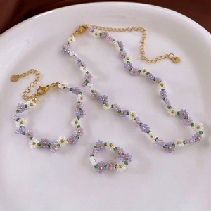 Detailed close-up of handmade purple and white beaded flower jewelry set on a ceramic plate