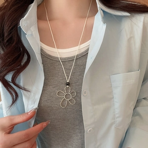 Close-up of minimalist silver hollow flower pendant with pearl on a cream necklace cord