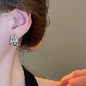 Detail of silver-tone crisscross hoop earrings with pavé zircons worn by a model
