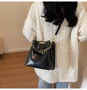 Crossbody black leather bucket bag with gold chain strap shown on a model's shoulder