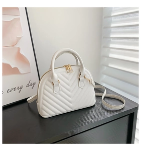 Detailed view of white shell bag featuring V-shaped quilting and gold metal hardware