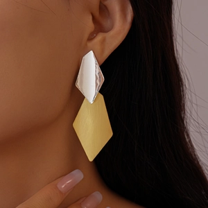 Detail of geometric rhombus earrings with silver and gold brushed metal finish worn by model