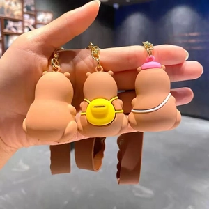 Trois porte-clés Capybara mignons en silicone brun avec breloques colorées tenus en main