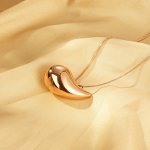 Close-up of a polished gold waterdrop pendant on a thin chain over silk fabric