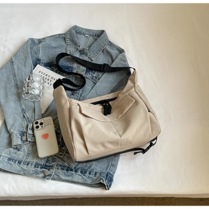 Detail of beige nylon crescent tote bag with wide strap on denim jacket background