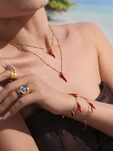 Close-up of model wearing gold layered necklaces with red pepper and clover charms