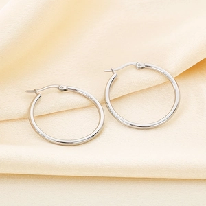 Detailed view of silver stainless steel hoop earrings on soft beige fabric background