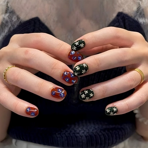 Detail of short round nails in dark red and green with floral patterns and sequins