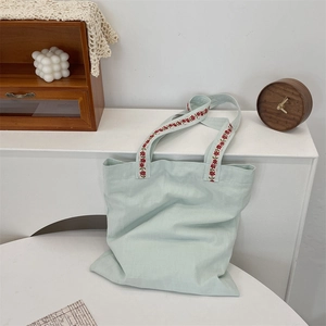 Détail du sac cabas en toile vert menthe avec broderie florale rouge sur la bandoulière