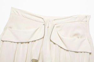 Detailed shot of cream mini skirt featuring silver beaded trim and pleated pocket design