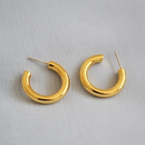 Detail shot of chunky 18k gold plated C-shaped geometric earrings on a fabric background