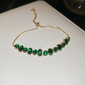 Détail d'un bracelet doré ajustable avec zircons verts ovales sur cuir blanc