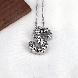 Detail view of silver S-letter pendant with unique textured grooves on white fabric
