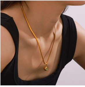 Close-up of golden geometric sphere pendant necklace with green inlay on snake chain