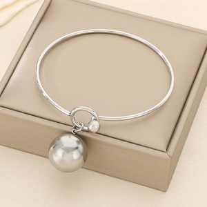 Close-up of polished silver bangle with hollow ball pendant on a beige jewelry box