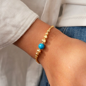 Close-up of 18K gold beaded bracelet with a blue stone bead worn on a model's wrist
