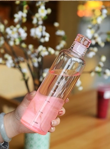 Close-up of glass water bottle with time markers being held against floral background