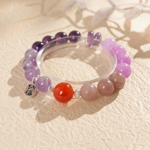 Detail of beaded gemstone bracelet with silver Na Fu charm on textured sand background