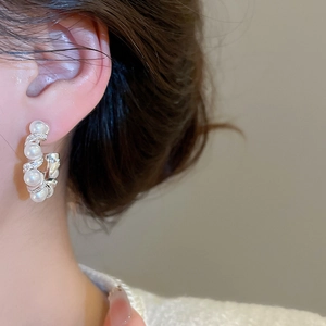 Detail of C-shaped hoop earrings featuring white pearls and micro-set cubic zirconia stones