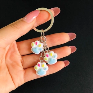 Handheld display of cute colorful resin cat paw keychains with metal rings on black backdrop