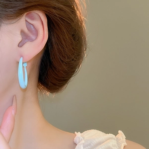 Close-up of light blue enamel C-shaped hoop earring worn by a model in soft lighting