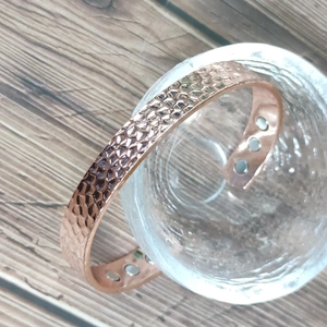 Koperen armband met golfpatroon textuur en magnetische uiteinden op een houten tafel
