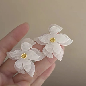 Detail shot of white layered floral earrings with gold center beads in a soft light