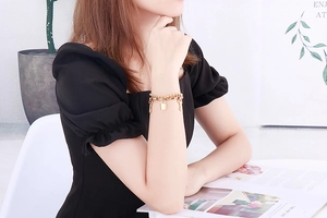 Detailed close-up of a double-layered gold lock and key pendant bracelet on a model wrist