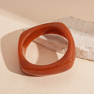 Macro detail of the irregular amber resin geometric bangle on a warm textured background