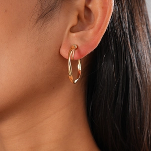 Close-up of golden metallic twisted rope hoop earring worn on model's ear