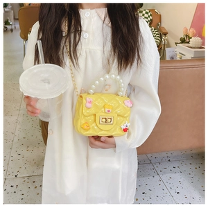 Detail of yellow quilted crossbody bag with pearl handle and cartoon charms