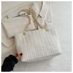 Detailed view of beige woven tote bag featuring elegant gold chain straps and leather base
