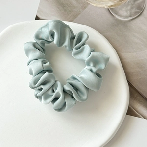 Gros plan d'un chouchou en satin bleu clair avec éclat soyeux sur une assiette blanche