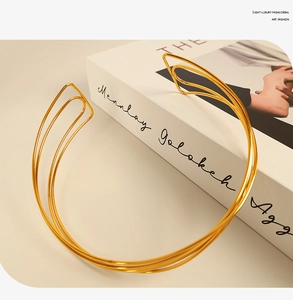 Artistic gold multi-layer choker necklace resting on a white book in soft natural light