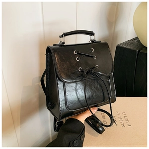 Detail of glossy black PU leather backpack featuring lace-up design and top handle