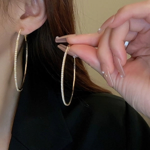 Close-up of a large gold hoop earring with sparkling white rhinestones on model
