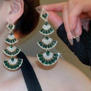 Detail of layered fan-shaped gold earrings with emerald green teardrop stones and zircon