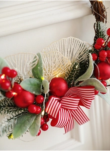 Detail of Christmas wreath with red berries, pine leaves, striped bow and warm LED lights