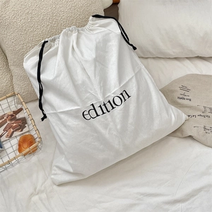 Minimalist cotton linen drawstring storage bag with black text on a clean white bed