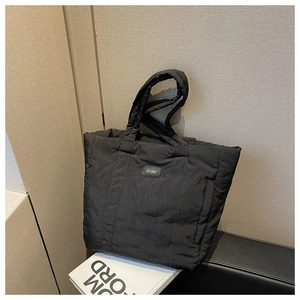 Detail shot of a black quilted nylon tote bag placed on a book against a textured wall