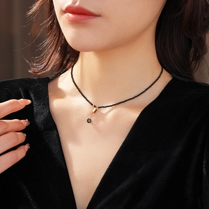 Close-up of model wearing a black bead necklace with a gold and black gemstone pendant
