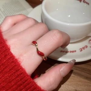 Detail view of gold-plated wavy ring with red enamel finish on female hand