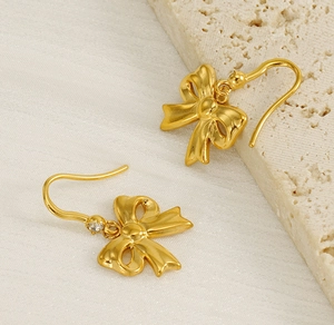Macro detail of 18K gold bow earrings with sparkling zircon and glossy metallic texture