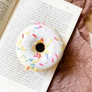 Detail of 3D donut phone grip with white frosting and sprinkles on a book background