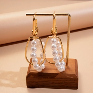 Macro detail of geometric gold earrings with pearls on a minimalist jewelry stand