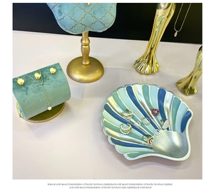 Flat lay of shell-shaped jewelry tray and green velvet display pad with gold necklace stand