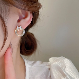 Macro shot of gold-plated earring with cubic zirconia and central white enamel H-logo