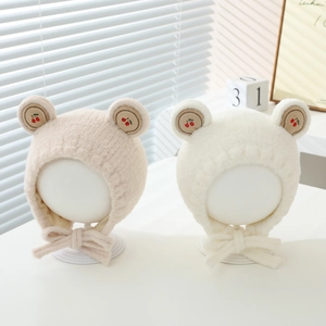 Détail de bonnets en peluche pour bébé avec broderie cerise et oreilles d'ours en beige