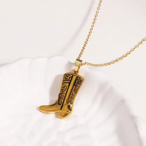 Goldene Cowboy-Stiefel Halskette aus Titanstahl auf einem weißen Muscheltablett