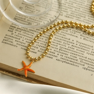 Detail of orange starfish pendant with gold beaded chain resting on vintage book pages